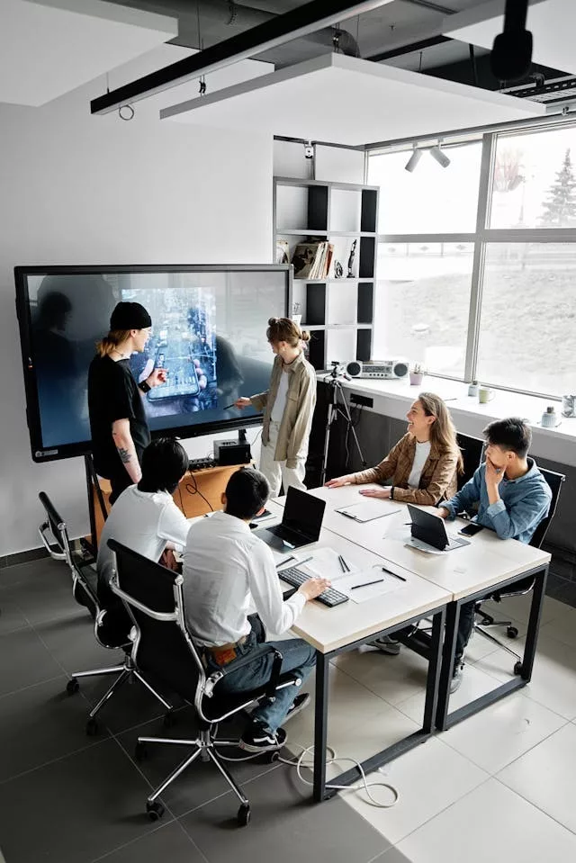 Grupo de seis personas en una sala de reuniones moderna observando una pantalla interactiva durante una presentación colaborativa sobre inteligencia artificial en el trabajo, con ordenadores