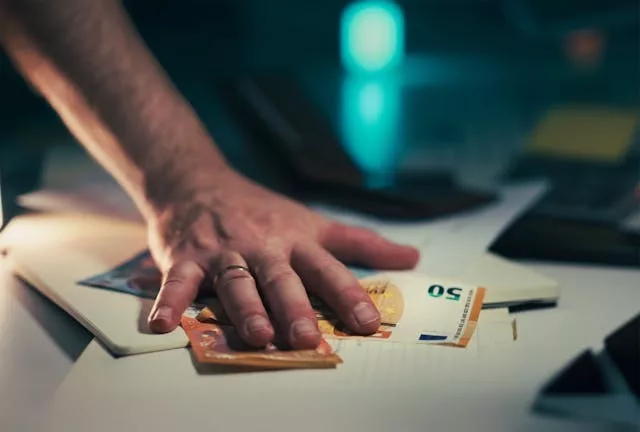 Primer plano de una mano apoyada sobre billetes de euro y una tarjeta bancaria encima de una mesa blanca junto a dispositivos electrónicos desenfocados, ilustrando cuánto gana un especialista en inteligencia artificial y el contexto salarial del sector tecnológico.
