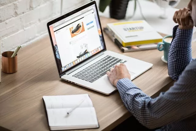 Profesional adulto trabajando concentrado con un portátil sobre un escritorio de oficina, con una taza de café y cuadernos junto al ordenador.