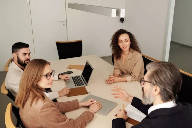 Equipo de adultos profesionales sentados alrededor de una mesa de sala de conferencias moderna, con laptops y documentos, discutiendo una estrategia empresarial.