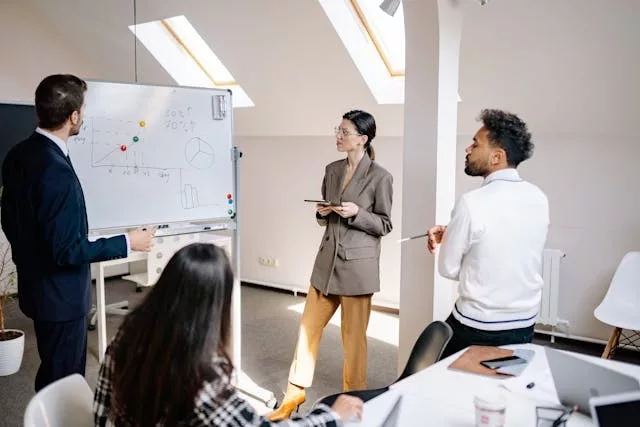 Grupo de profesionales adultos alrededor de una mesa con gráficos y una presentación proyectada durante una reunión de planificación estratégica en una oficina moderna sobre cómo elaborar una estrategia de IA generativa para tu empresa.