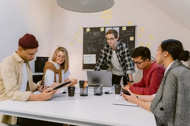 Grupo de profesionales adultos alrededor de una mesa con gráficos y una presentación proyectada durante una reunión de planificación estratégica en una oficina moderna sobre cómo elaborar una estrategia de IA generativa para tu empresa.